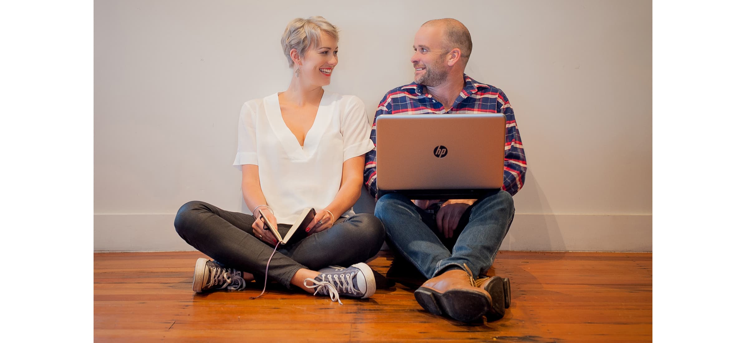 The Experience Collective founders Rosie and Nick Rogers sitting beside each other on a wooden floor, smiling.
